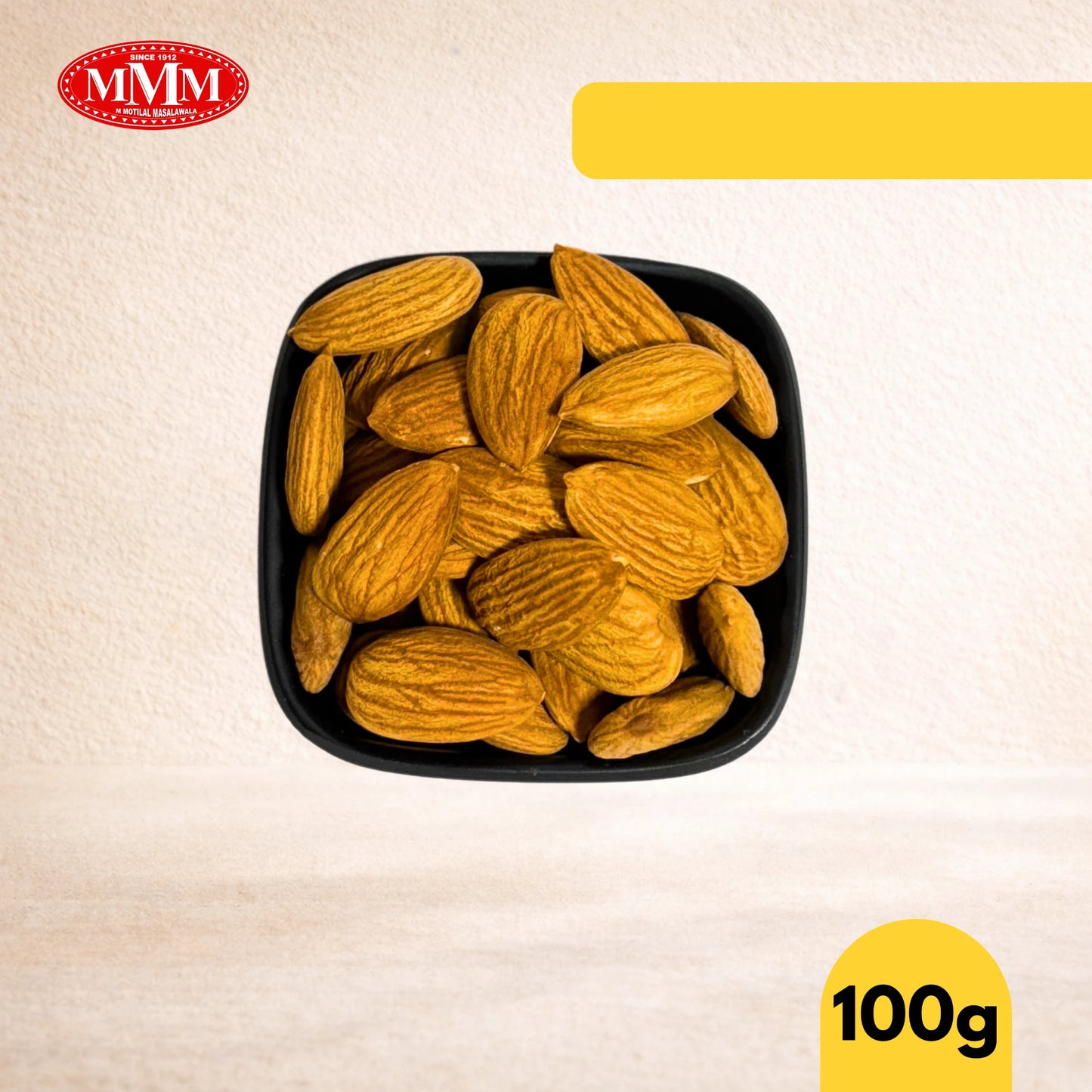 Black square bowl filled with American almonds on a beige background, featuring the MMM logo.