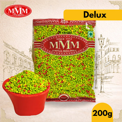 MMM Delux packet of green colored mukhwas with a small bowl filled with spices on a decorative background.